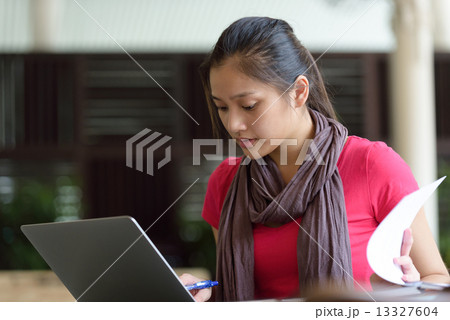 One young pan asian female student studying hard for examination in campus cafe 13327604