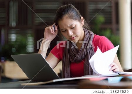 One young pan asian female student studying hard for examination in campus cafe 13327629