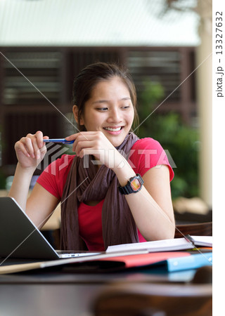 One young pan asian female student studying hard for examination in campus cafe 13327632