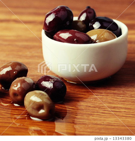 different olives in white bowl on wooden board 13343380