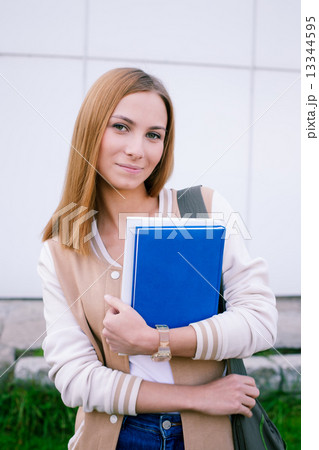 Student standing with book and looking at camera 13344595