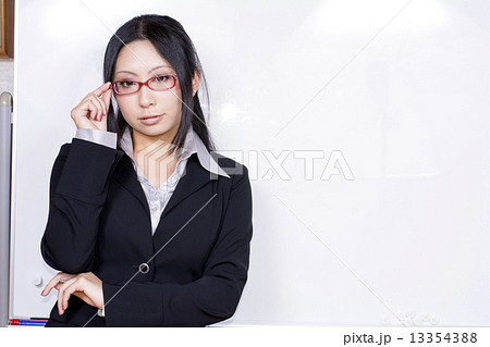 ホワイトボードの前で眼鏡にさわるスーツ姿の女性の写真素材
