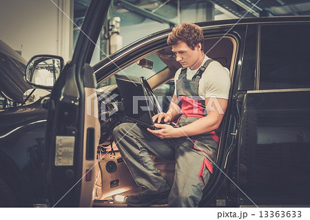Serviceman making car diagnostics with laptop in a workshop 13363633