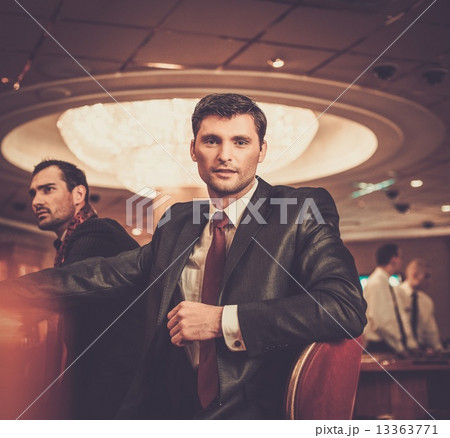 Two fashionable men in suits behind table in a casino Two fashionable men in suits behind table in a casino 13363771