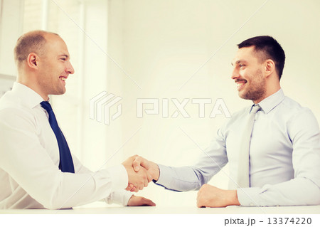 two smiling businessmen shaking hands in office two smiling businessmen shaking hands in office 13374220