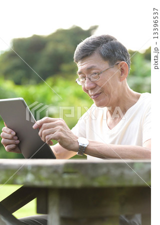 One male chinese elderly using iPad in the park 13396537