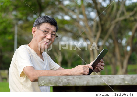 One male chinese elderly using iPad in the park One male chinese elderly using iPad in the park 13396548