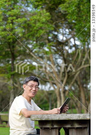 One male chinese elderly using iPad in the park 13396549