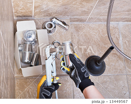 plumber repairs sink trap in bathroom 13449567