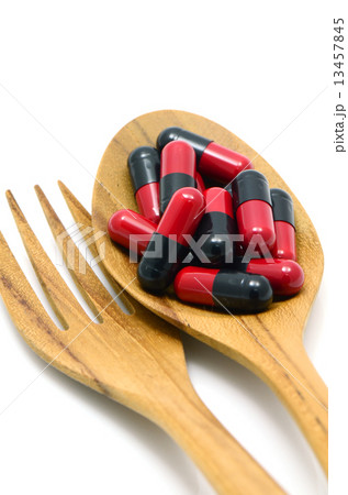 Oral medication red and black capsules in a table spoon on white background. Oral medication red and black capsules in a table spoon on white background. 13457845