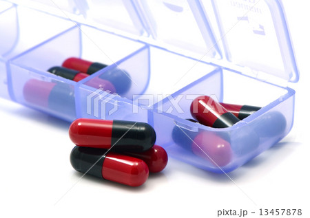 Oral medication red and black capsules in separated unit-dose box on white background. Oral medication red and black capsules in separated unit-dose box on white background. 13457878