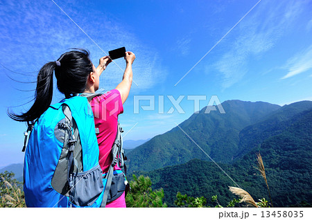 hiking woman taking photo with phone at mountain peak  13458035