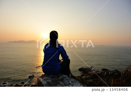 hiking woman sit on mountain rock watching the sunrise at the sea 13458408