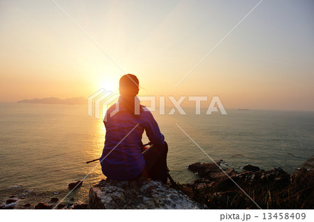 hiking woman sit on mountain rock watching the sunrise at the sea 13458409