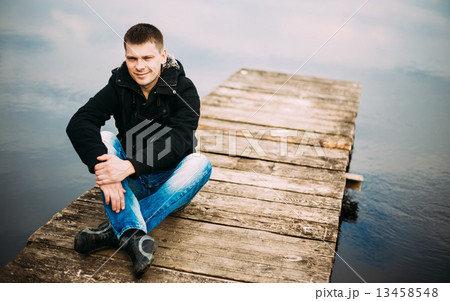 Young handsome man sitting on wooden pier, relaxing, thinking. Young handsome man sitting on wooden pier, relaxing, thinking. 13458548
