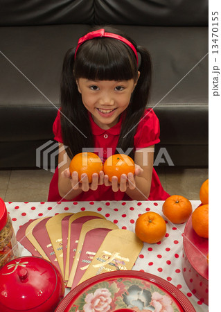 Young cheerful Asian girl holding a pair of orange sybmolizes wreath during Lunar / Chinese New Year 13470155