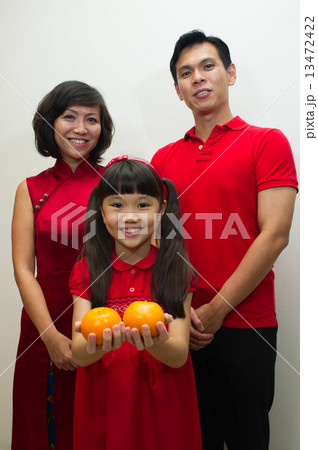 Portrait of a family of three Asian in red posing with mandarin oranges for Lunar / Chinese new year 13472422
