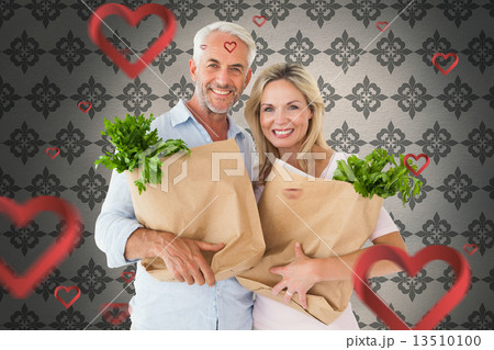 Composite image of happy couple carrying paper grocery bags 13510100