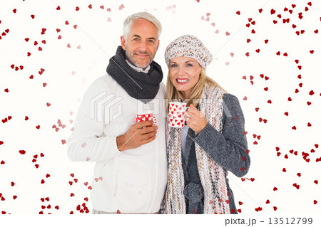 Composite image of happy couple in winter fashion holding mugs 13512799