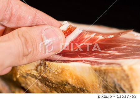 Caucasian man hand takes slices from Serrano ham 13537765
