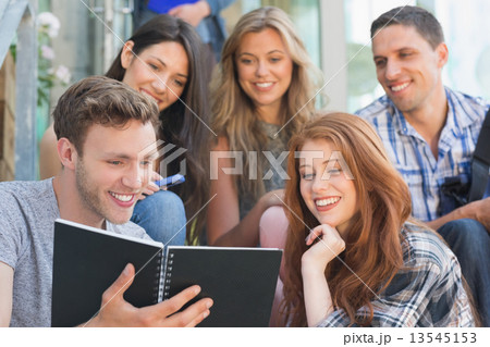 Happy students looking at book outside on campus Happy students looking at book outside on campus 13545153