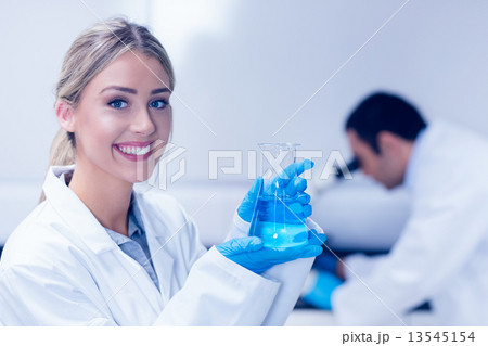 Science student holding blue chemical in beaker 13545154