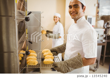 Baker smiling at camera taking rolls out of oven Baker smiling at camera taking rolls out of oven 13545240
