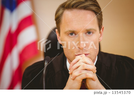 Unsmiling judge with american flag behind him Unsmiling judge with american flag behind him 13545370