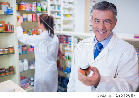 Smiling pharmacist holding a box of pills Smiling pharmacist holding a box of pills 13545687