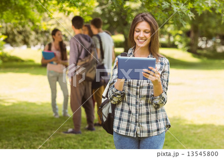 Smiling student with a shoulder bag and using tablet computer 13545800
