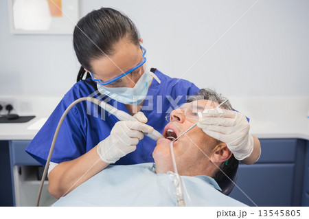 Dentist examining a patient with suction hose 13545805