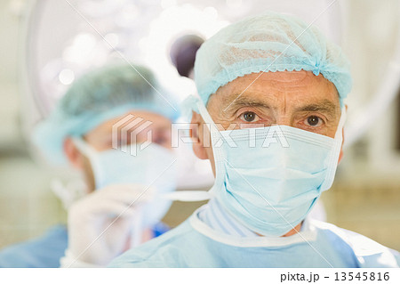 Young surgeon tying older surgeons mask 13545816