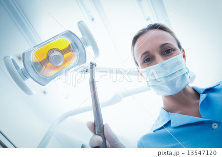 Female dentist in surgical mask holding dental tool 13547120