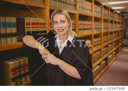 Smiling lawyer leaning on shelf 13547306