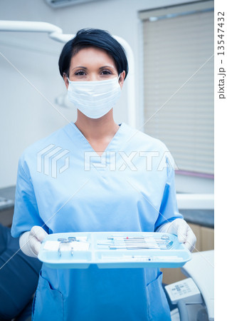 Female dentist in blue scrubs holding tray of tools Female dentist in blue scrubs holding tray of tools 13547432