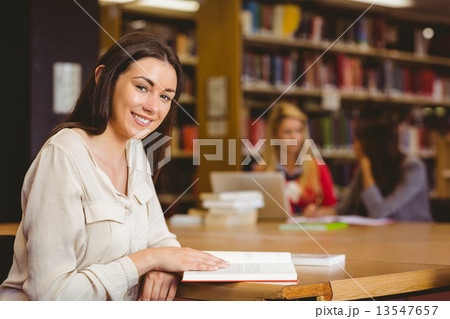 Smiling student sitting at desk reading text book Smiling student sitting at desk reading text book 13547657