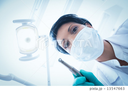 Female dentist in surgical mask holding dental drill 13547663