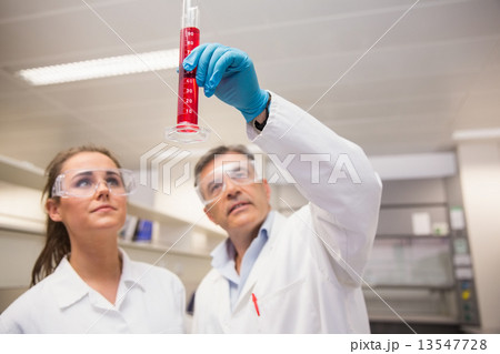 Pharmacists looking at beaker of red liquid 13547728