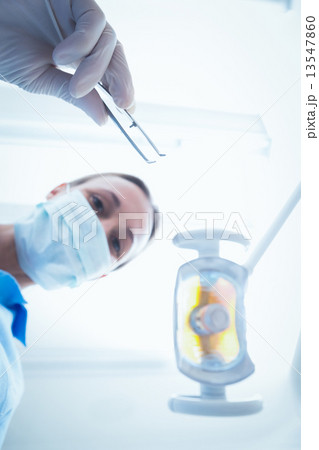Female dentist in surgical mask holding dental tool 13547860