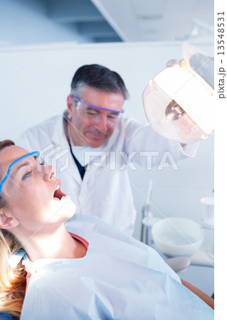 Dentist examining a patients teeth in chair under bright light 13548531
