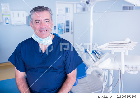 Dentist smiling at camera beside chair 13549094