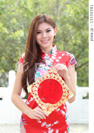 Chinese New Year Sign held by Woman wearing Chenogsam in front of green tree 13550381