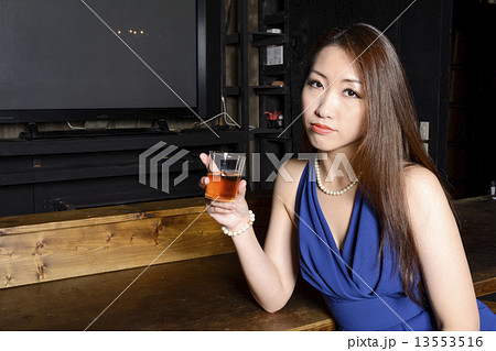 カウンターでグラスを持つカクテルドレスの女性 13553516