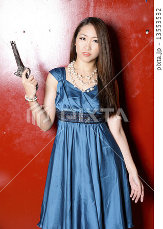 赤い壁の前に立って銃を持つカクテルドレスの女性 赤い壁の前に立って銃を持つカクテルドレスの女性 13553532