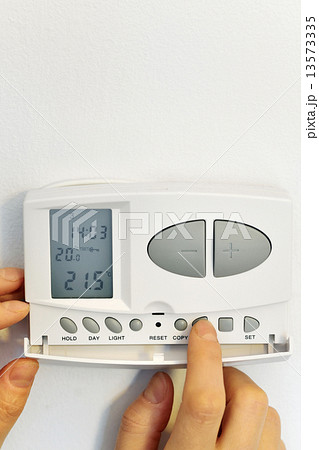 hand pressing button on digital thermostat 13573335