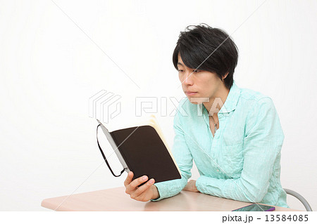 椅子に座って手帳を触る男性 13584085
