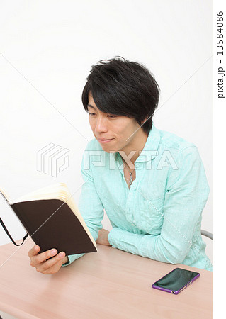 椅子に座って手帳を触る男性 13584086