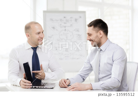 two smiling businessmen with laptop in office two smiling businessmen with laptop in office 13595512