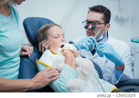 Dentist examining girls teeth with assistant 13602820