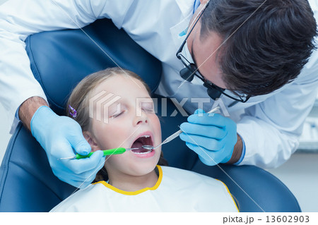 Male dentist examining girls teeth 13602903